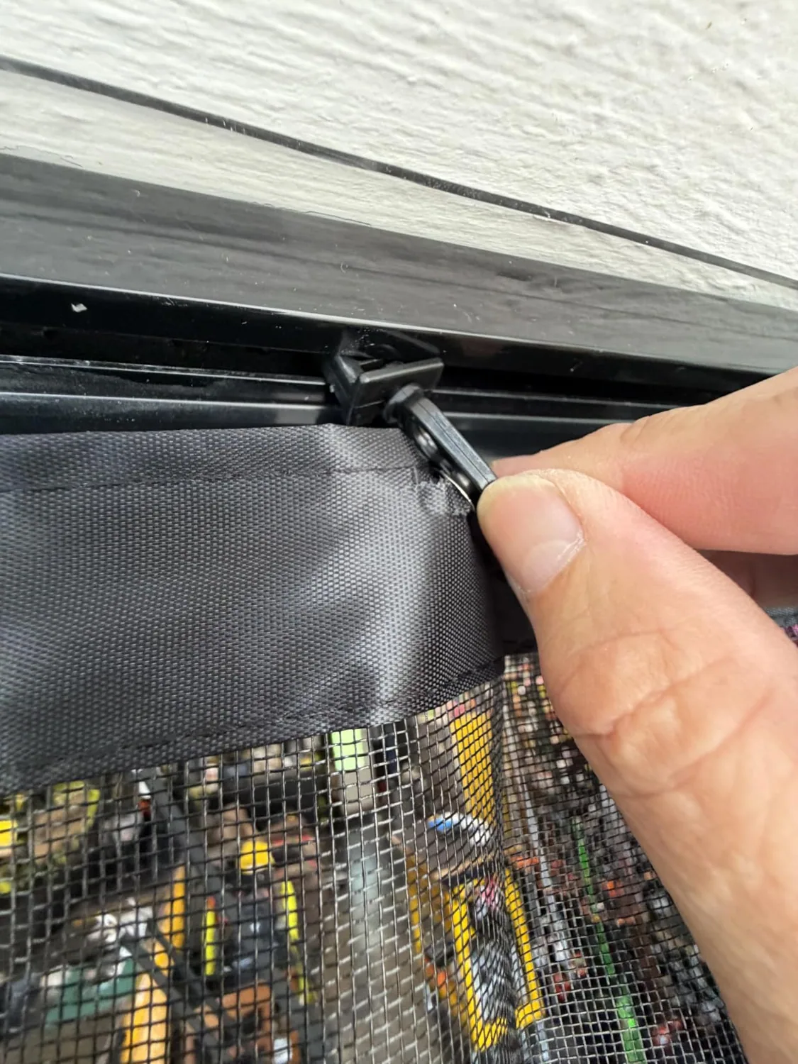 Buyer photo: fingers on a roller clip of a FEGO sliding garage door screen in its top track